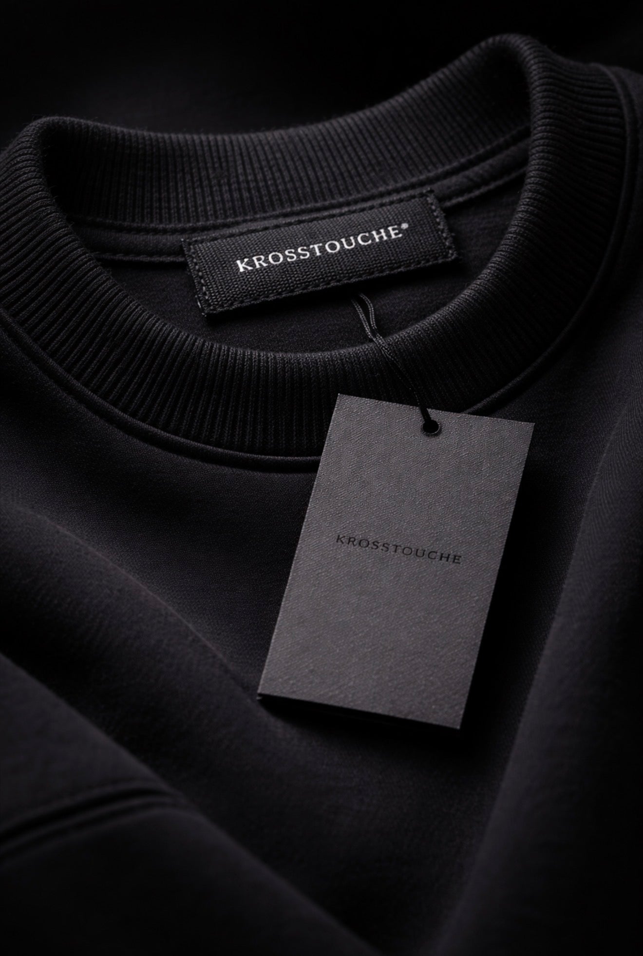 KROSSTOUCHE® black premium sweatshirt close-up showing woven neck label and branded hang tag