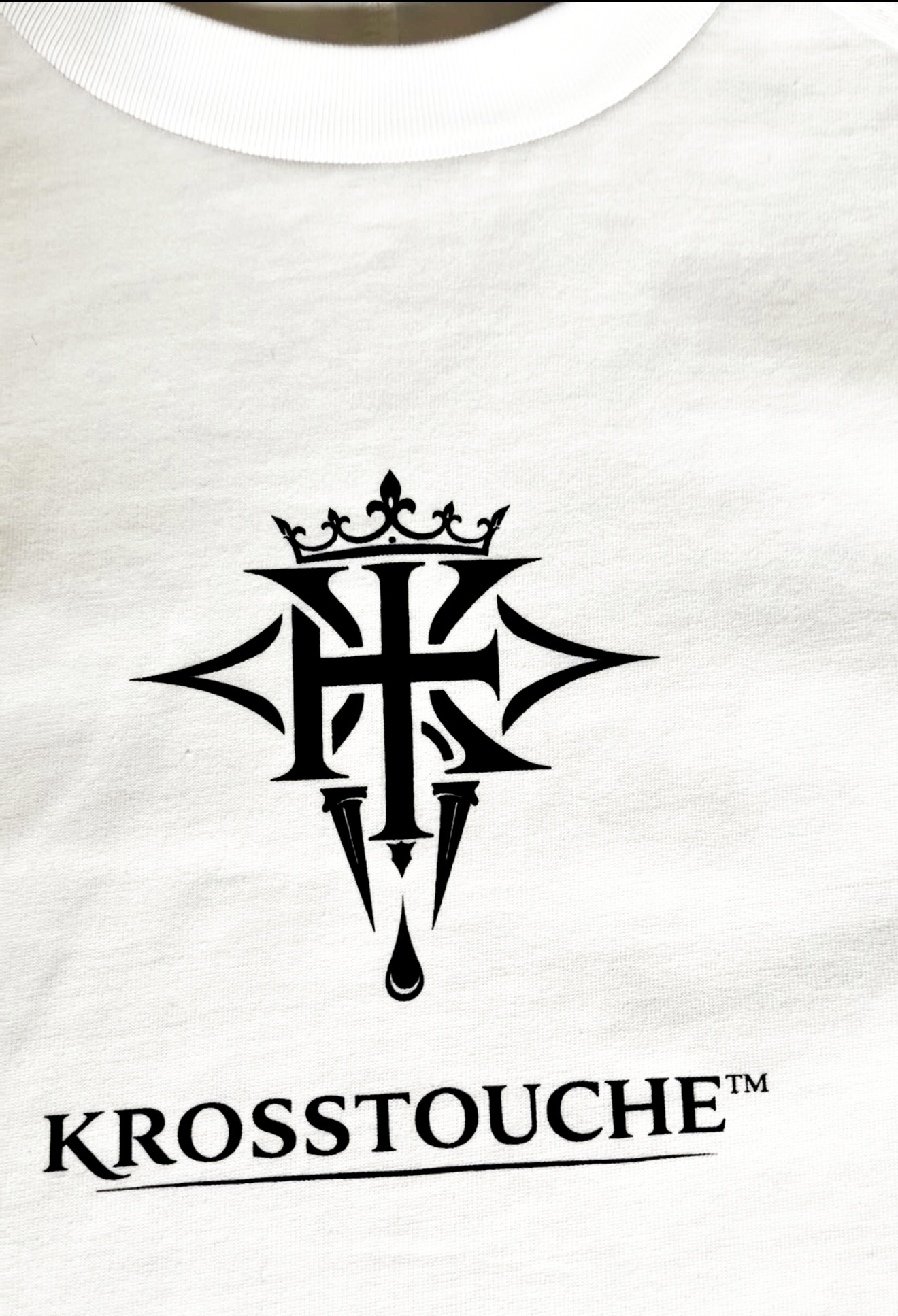 Close-up view of the KROSSTOUCHE® Signature Heavyweight T-Shirt in Optic White showing the black crest logo and chest print detail.